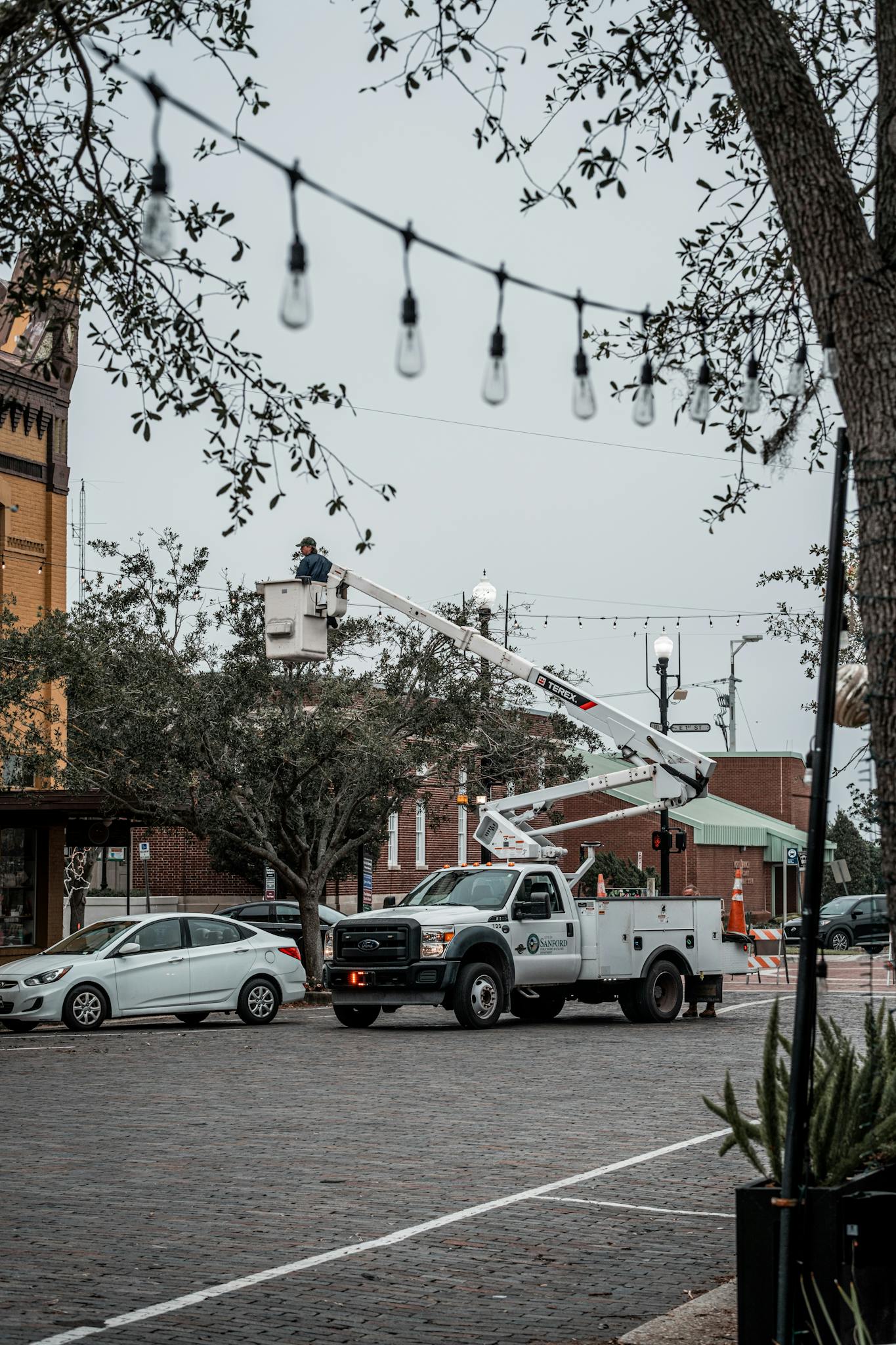 Utility worker on lift in a city street, setting up lights on a cloudy day.